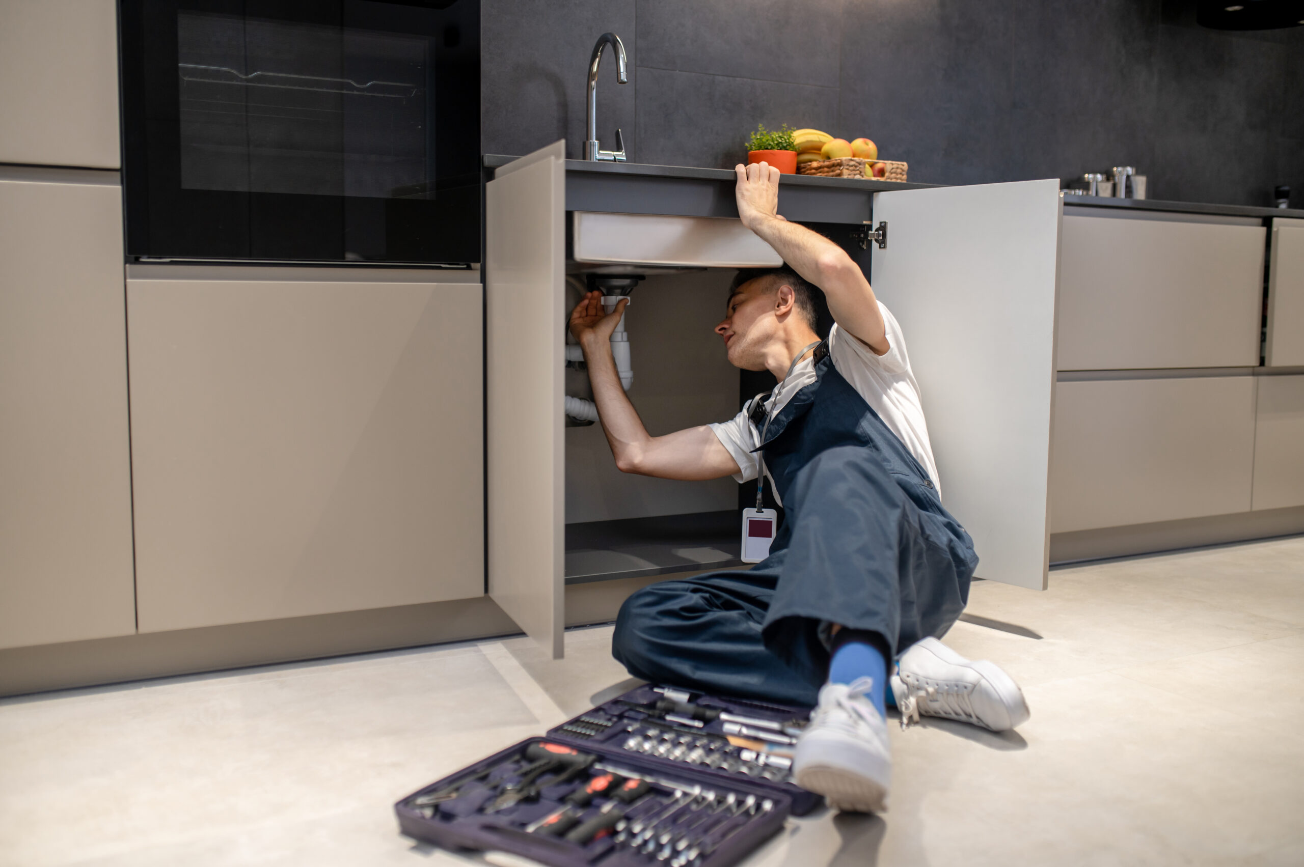 Man reclining inspecting pipe under kitchen sink Plumber in Oakville